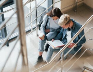 two college students sitting in a stairway reading.