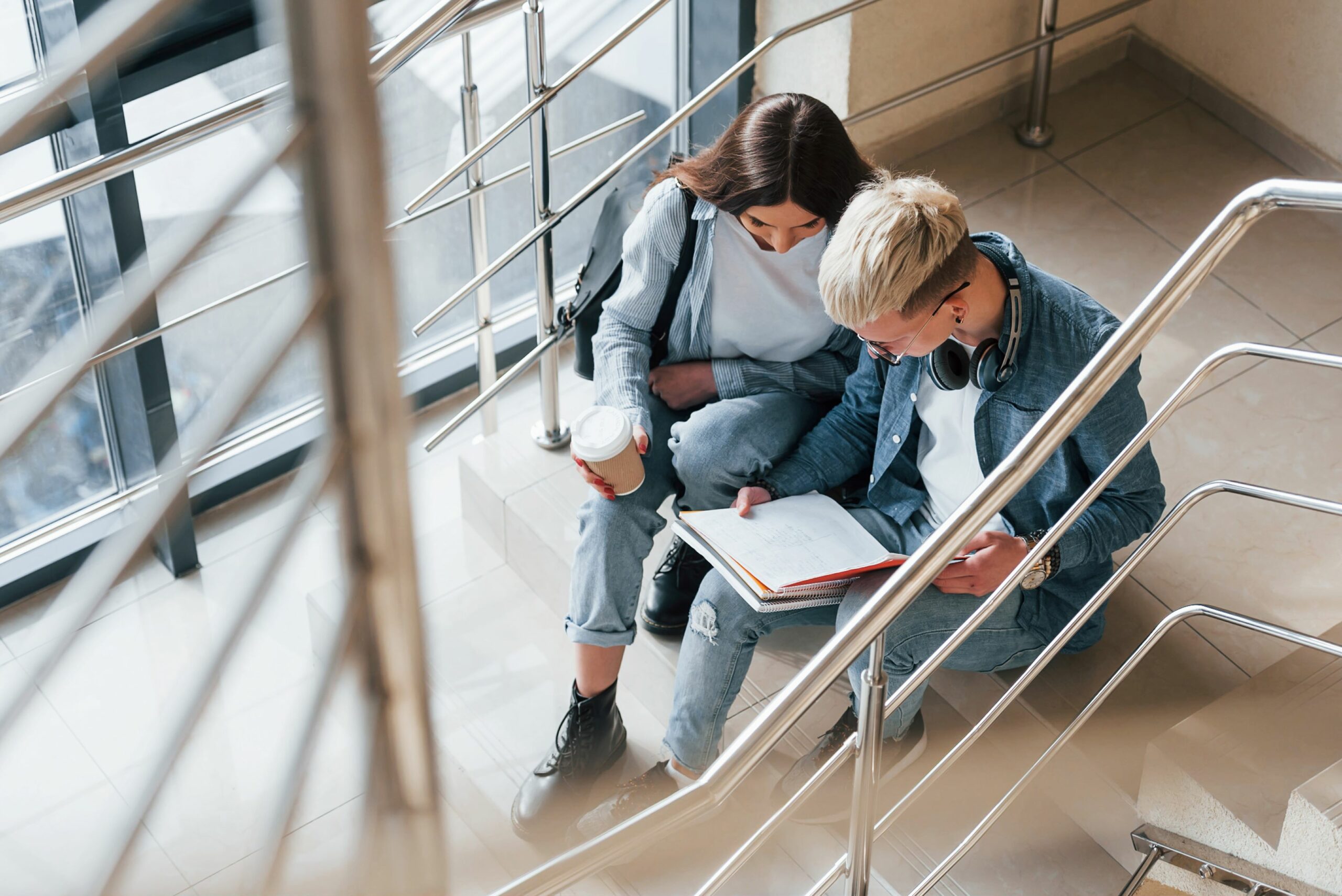 two college students sitting in a stairway reading.